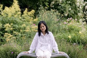Nhung Bohman, a certified hypnotherapist offering hypnosis in Gothenburg, sits calmly on a bench in a peaceful garden, ready to guide you on your healing journey