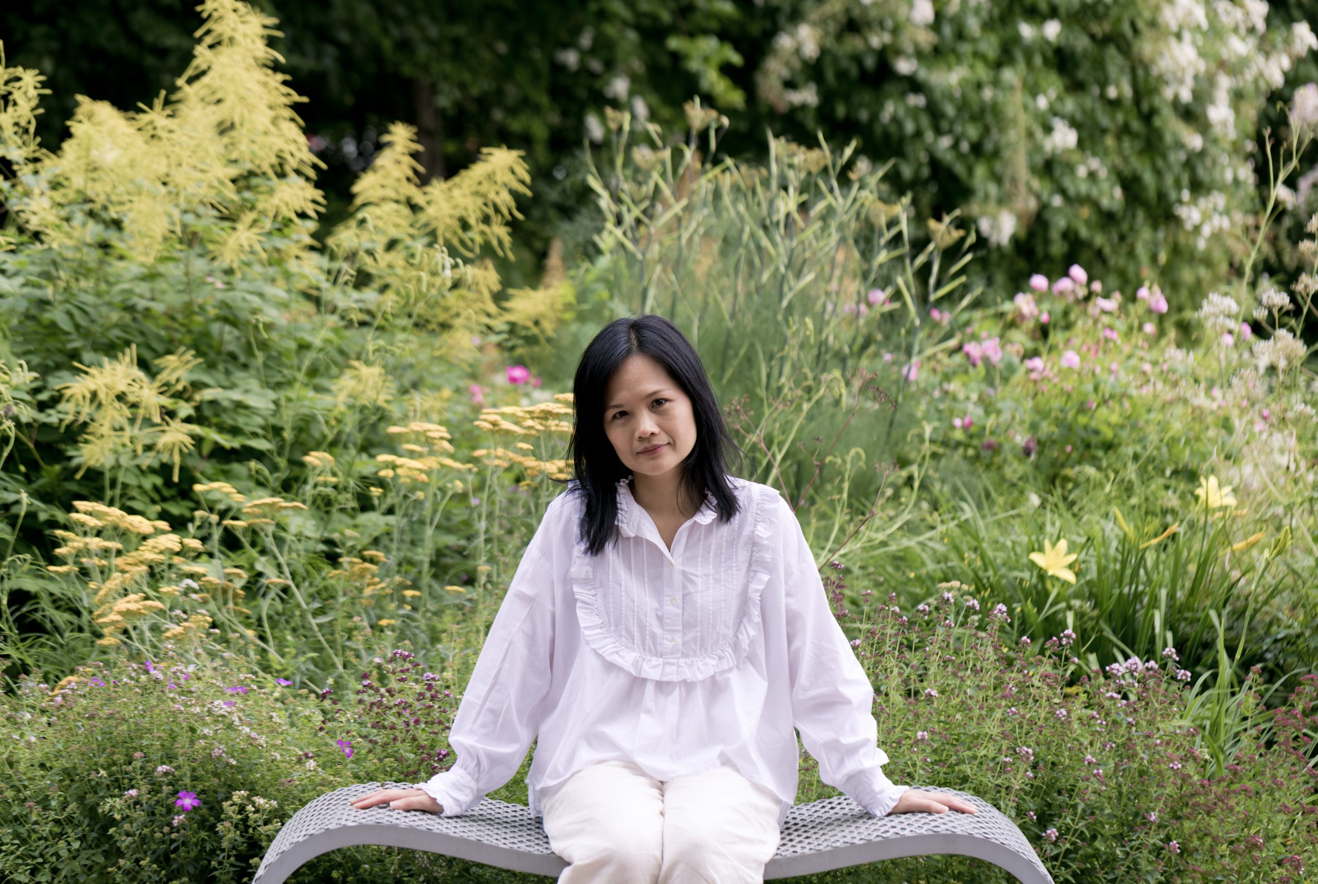 Nhung Bohman från Hypnoterapi Göteborg sitter på en bänk i en rofylld trädgård, en miljö som representerar det lugn som terapin kan ge